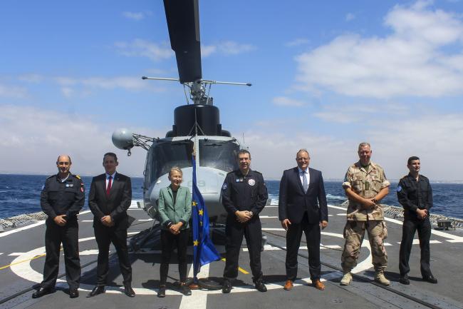 A group of officials and military personnel standing on the deck of a naval ship under a clear sky. Among them is Tiina Intelmann, Head of the EU Delegation to Somalia, accompanied by senior EUNAVFOR and EU mission representatives, including Alexander Borum, Advisor on Political and Security Affairs, Somalia.